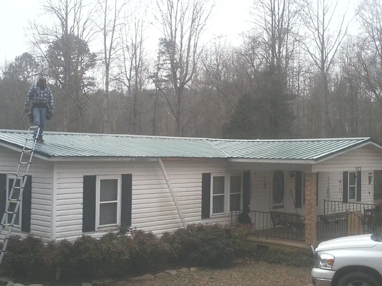 Worker on a ladder beside a new green metal roof on a ranch home in Stuarts Draft
