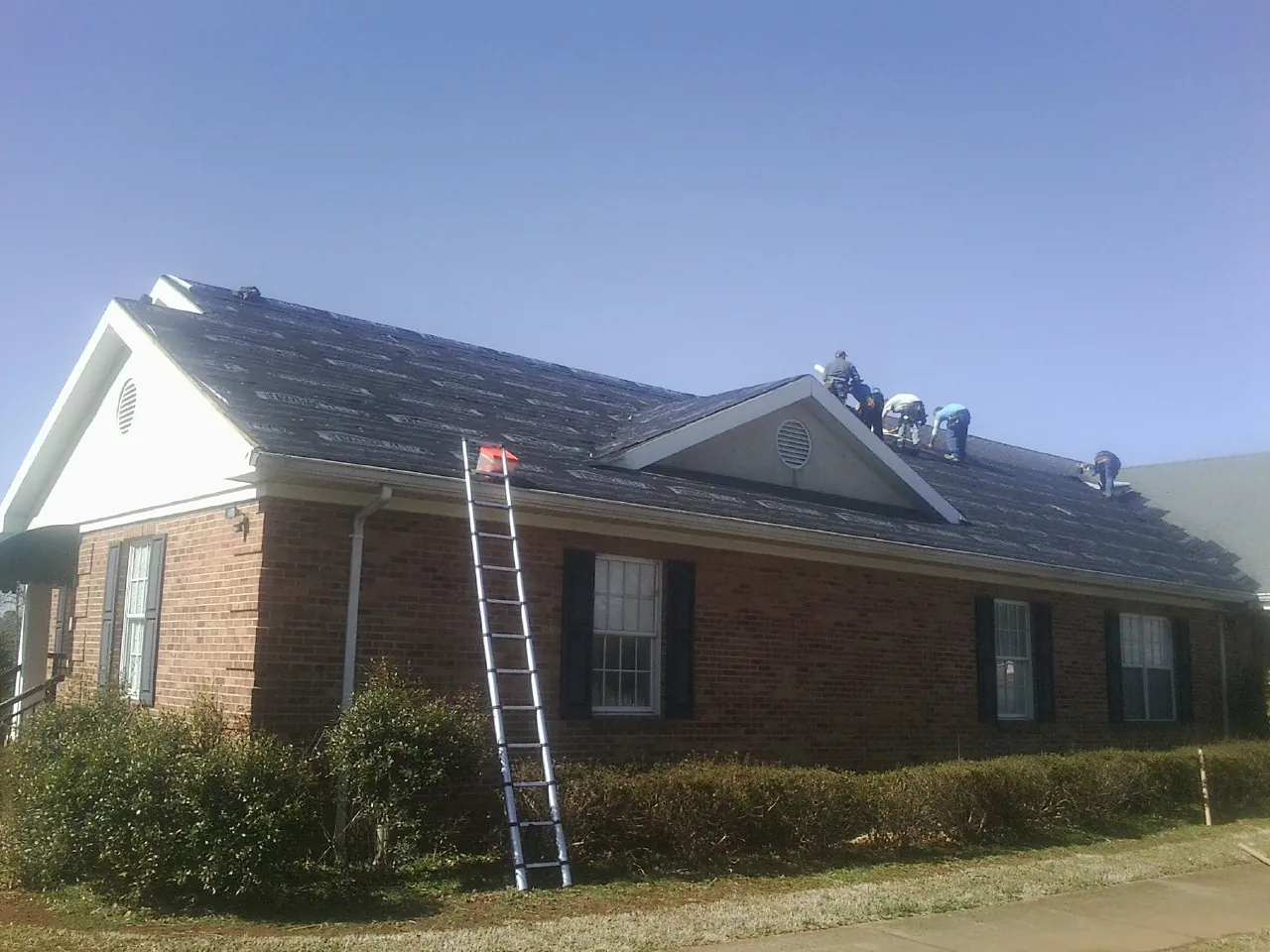 Crew tearing shingles off a brick ranch roof with a ladder set — Emergency Roof Repair work by our crew in Stuarts Draft