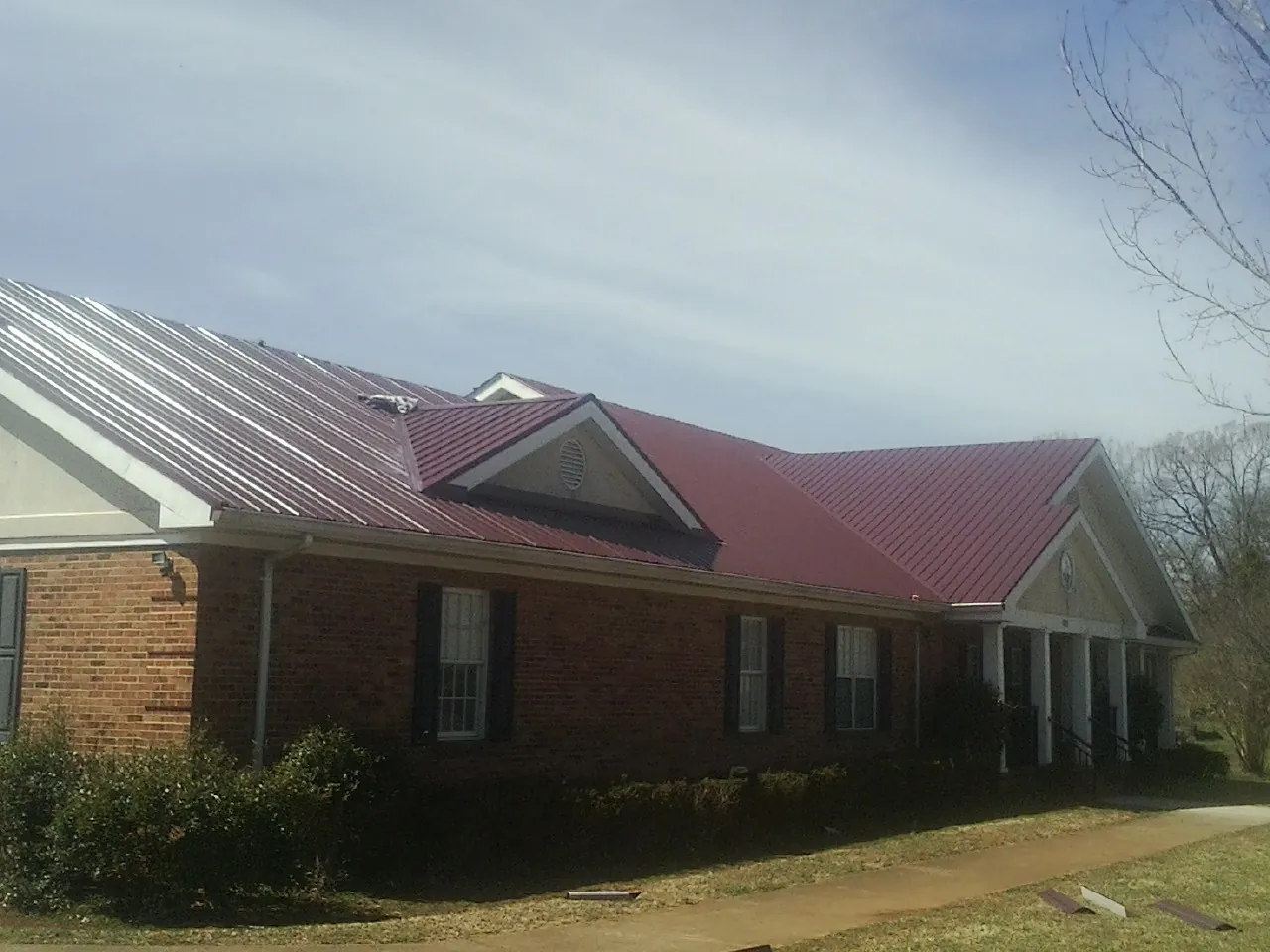 Red metal roof with gabled entries on a long brick building, from a Hail Damage Roof Repair job in Stuarts Draft