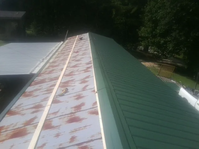 Old rusted panels beside newly installed green metal roofing — Wind Damage Roof Repair by Roofing Brothers in Stuarts Draft