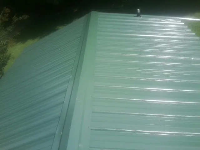 New green metal panels meeting at the ridge of a roof — Flat Roof Repair work by our crew in Stuarts Draft