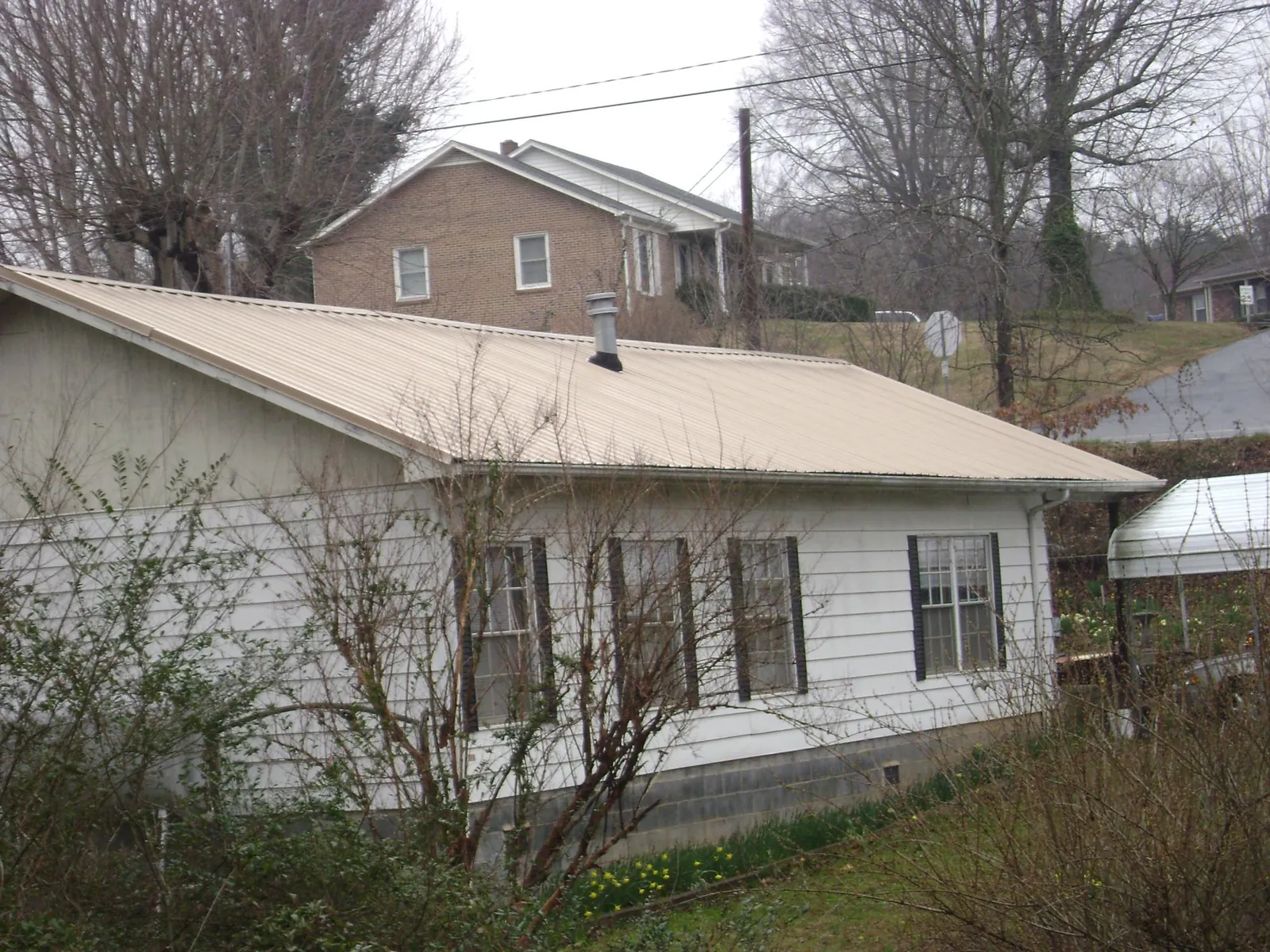 Tan metal roof on a white sided house set into a hillside — Commercial Roofing by Roofing Brothers in Stuarts Draft